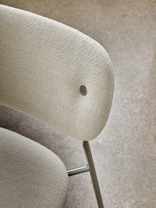 A detailed close-up of the fully upholstered Co Dining Chair, showing the textured cream Audo Bouclé fabric and chrome legs.