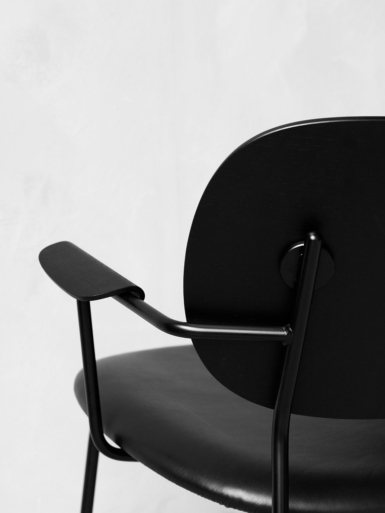 A black and white close-up of the Co Lounge Chair, highlighting the black wood armrest, round back, and slender metal frame.