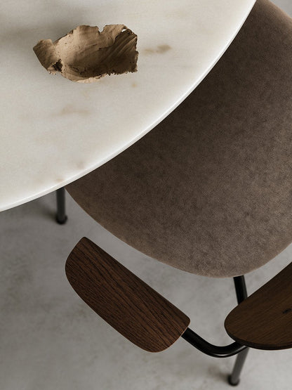 Overhead detail shot of the white marble Harbour Column Dining Table and brown upholstered Co Chair with dark wood armrests.