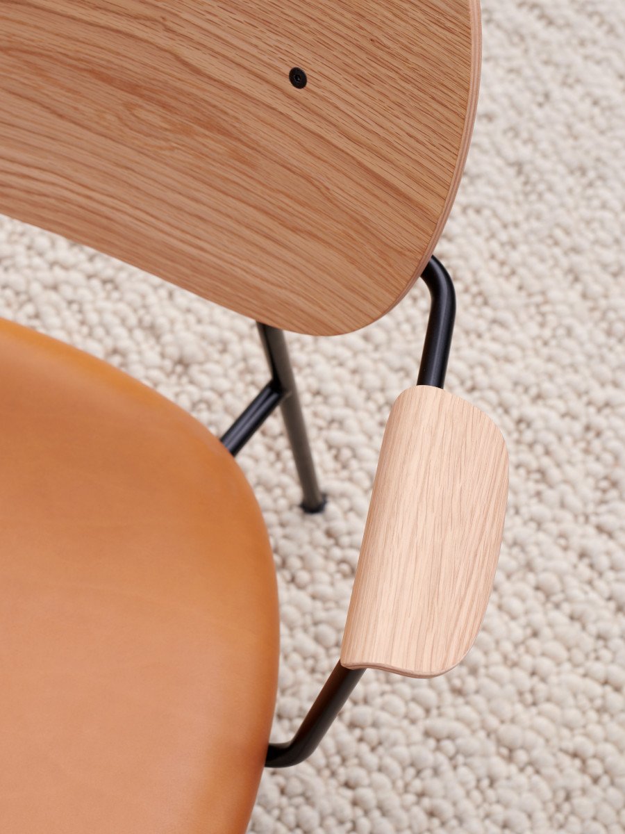 Close-up of the Co Lounge Chair with natural oak backrest, tan upholstered seat, and black metal frame on a textured rug.