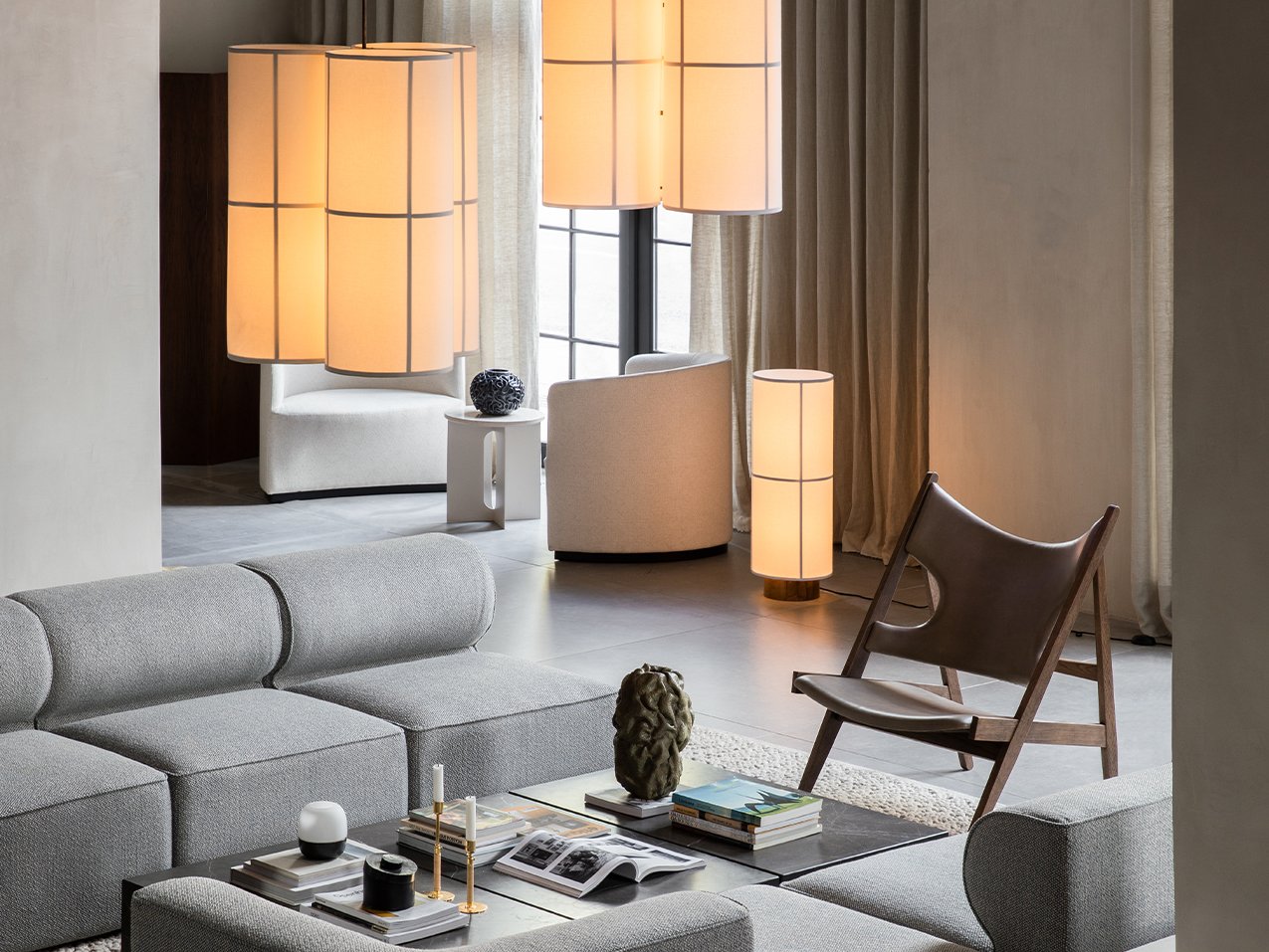 A modern living room with the illuminated Hashira Floor Lamp next to a brown leather chair and grey modular sofa.