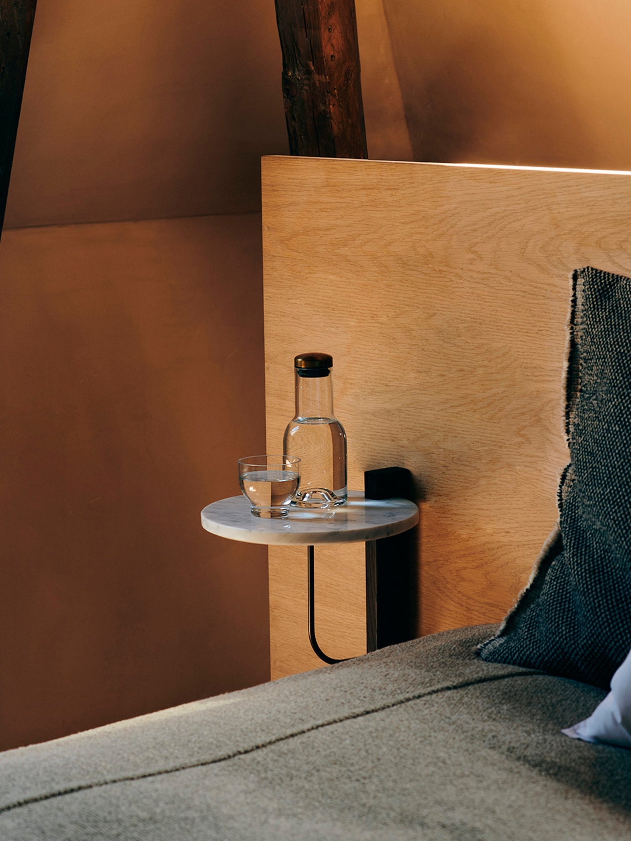 Corbel Shelf in white marble, mounted on a wooden headboard, functioning as a minimalist bedside table with a water bottle.