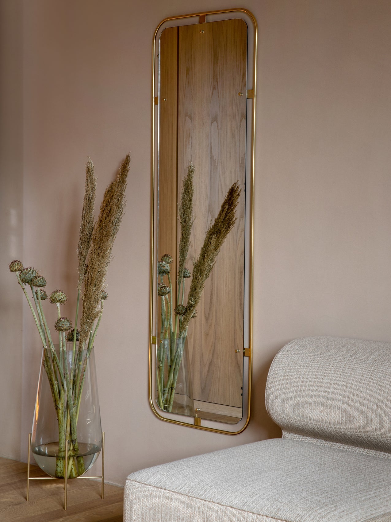 A light Eave Modular Sofa next to an Echasse Vase with dried flowers. A brass Nimbus Mirror hangs on the dusty pink wall.
