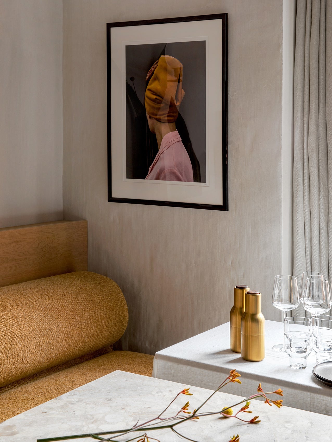 A corner setting with a mustard-yellow Eave Dining Sofa, a table set for dining, and a framed photograph on a light wall.