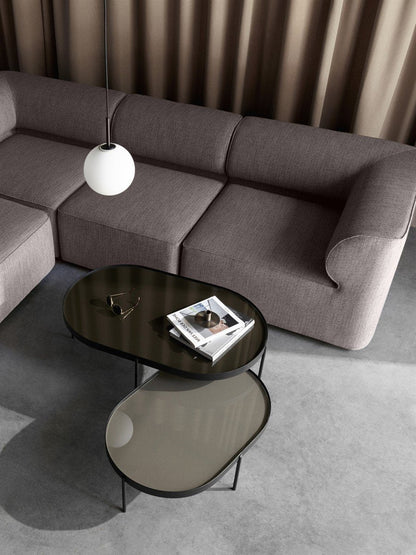 Overhead view of two oval NoNo Tables with dark glass tops placed in front of a grey Eave Modular Sofa in a minimalist room.