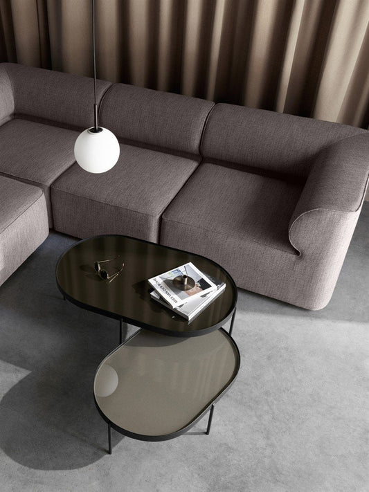 Overhead view of two oval NoNo Tables with dark glass tops placed in front of a grey Eave Modular Sofa in a minimalist room.