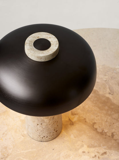 A close-up of the Reverse Table Lamp with a travertine stone base and black shade, resting on a stone Harbour Column Table.