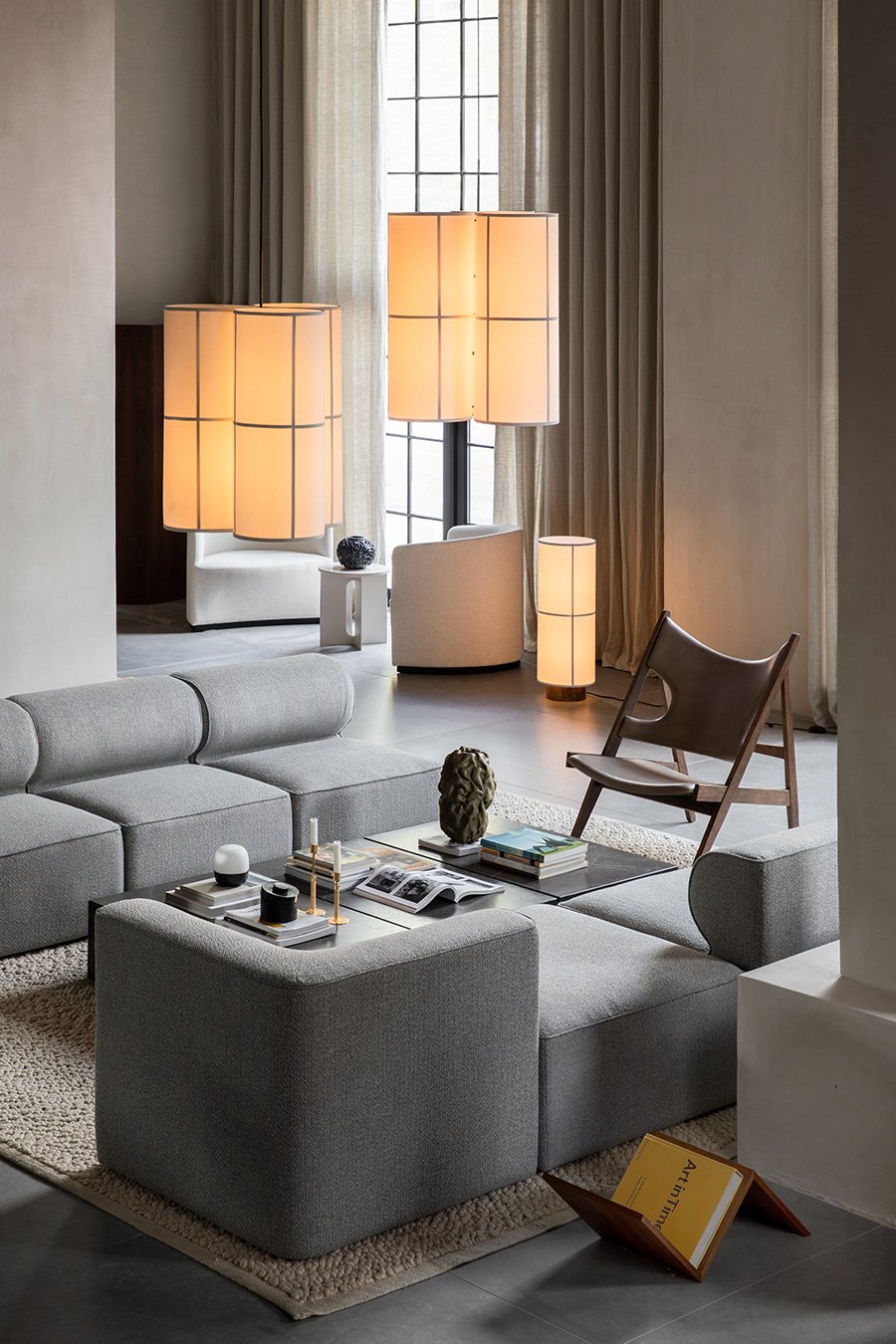 Modern living room with several illuminated Hashira Floor Lamps of different sizes, a grey sofa, and a leather lounge chair.
