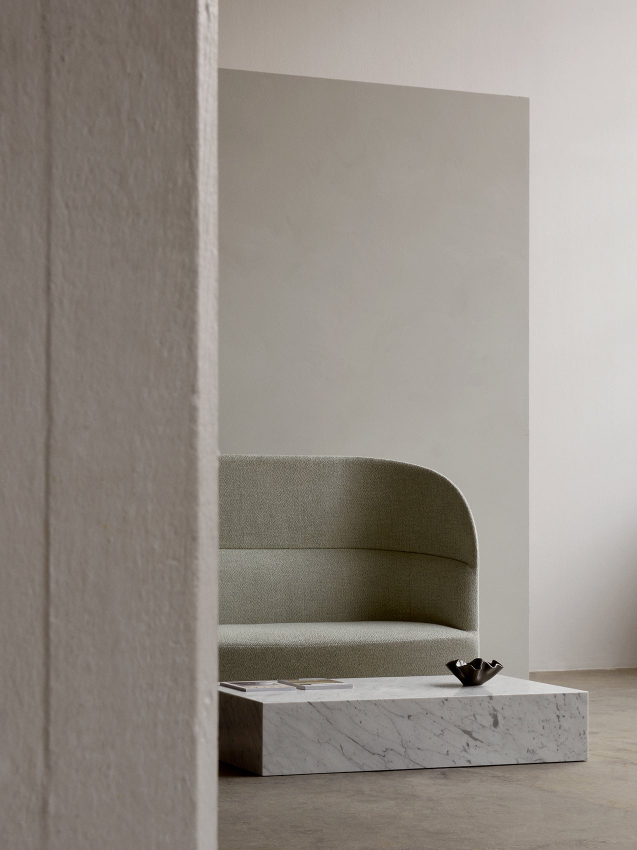 Side view of a light grey Tearoom Sofa, High Back in a minimal room. A marble coffee table holds a dark Fragilis Bowl.