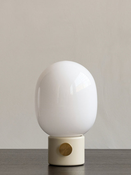 A front view of the JWDA Table Lamp, Small, with a light grey concrete base and brass dimmer, on a dark wooden table.