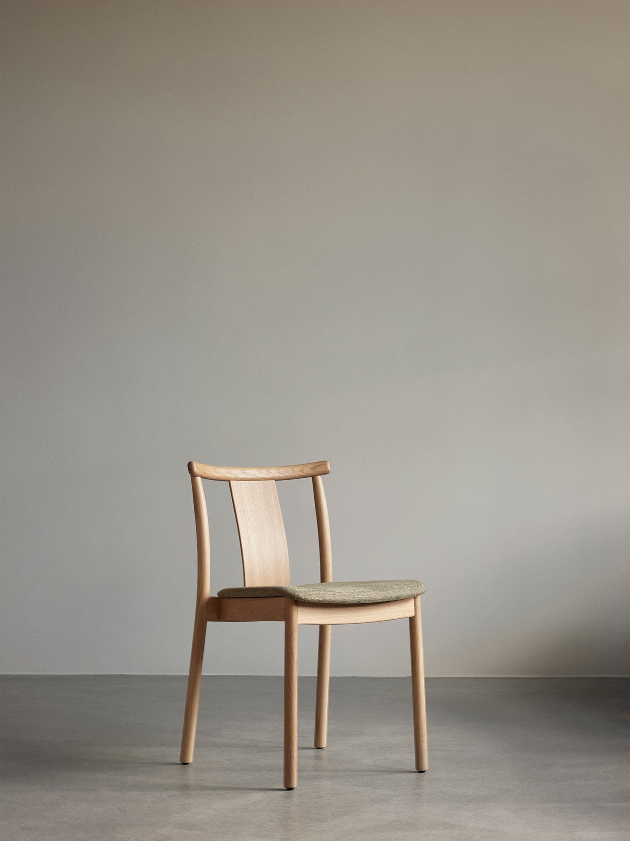 The Merkur Dining Chair in natural oak with a green fabric upholstered seat, shown front-on against a plain grey wall.