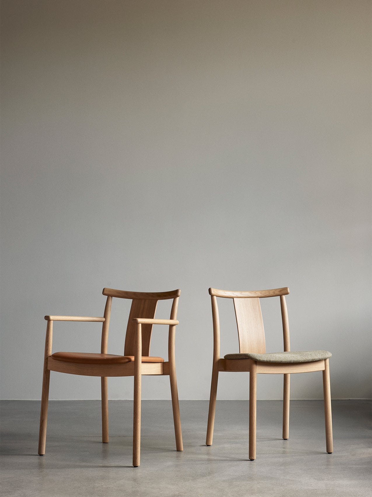 Two versions of the Merkur Dining Chair in light oak. One with armrests and a leather seat, and one with a fabric seat.