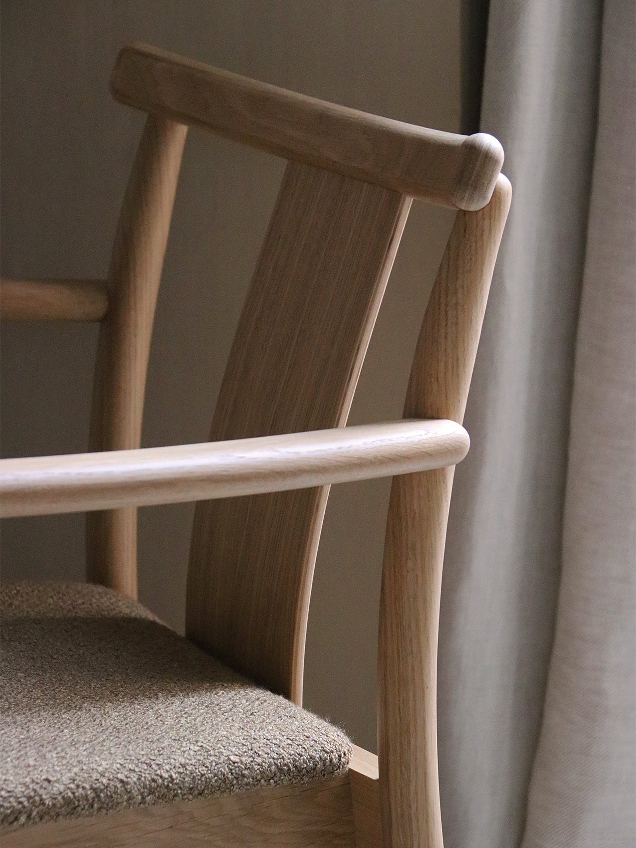 A detailed close-up of the Merkur Dining Chair with Armrests, showing the light oak wood grain on the backrest and armrest.