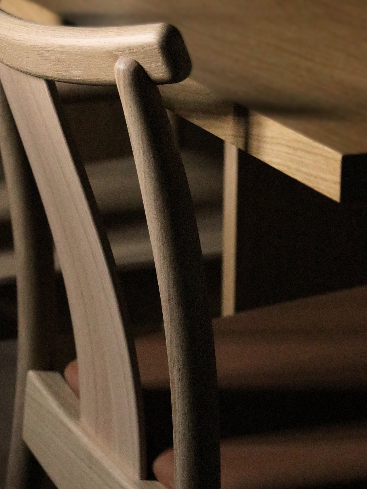 Close-up of the Merkur Dining Chair in natural oak, showing the detailed joinery of the curved backrest next to a table.