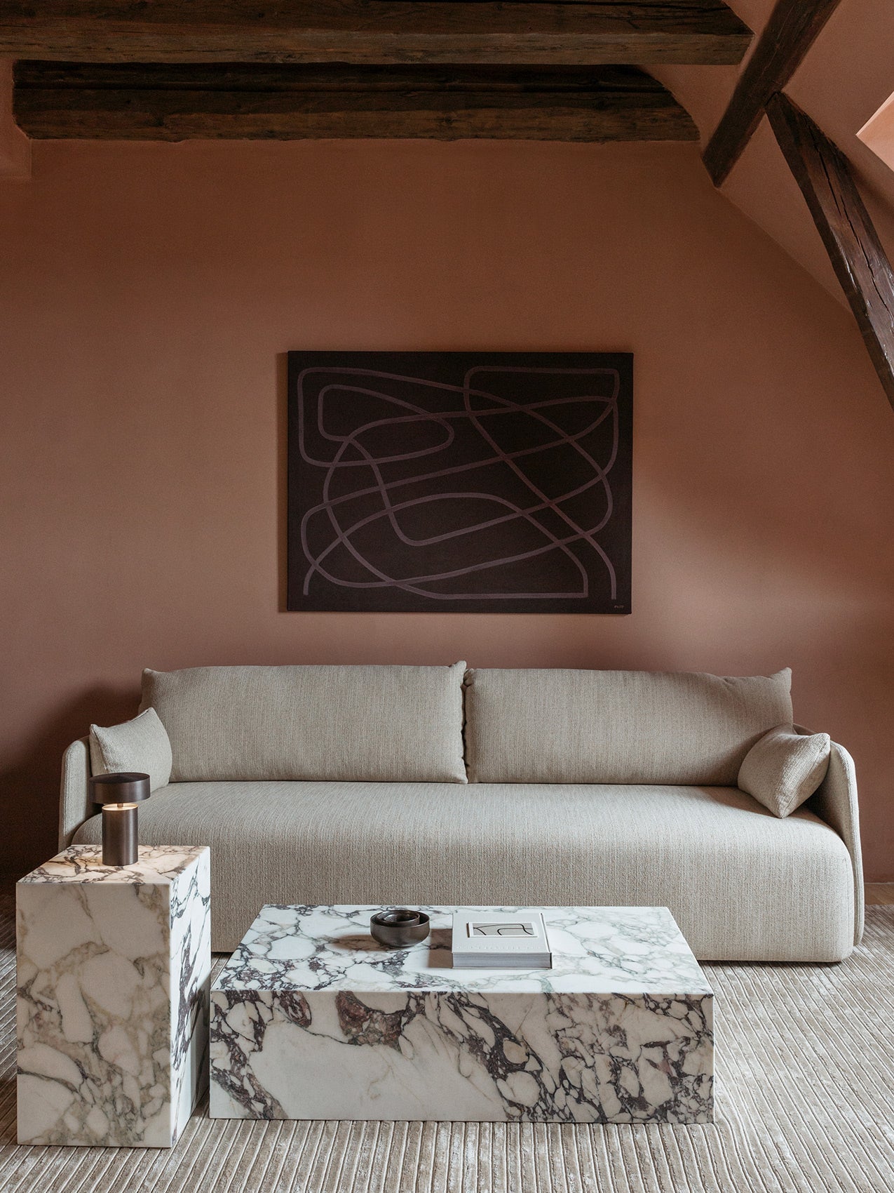 A light grey Offset Sofa against a terracotta wall below an abstract painting, with marble Plinth tables and a Column Lamp.