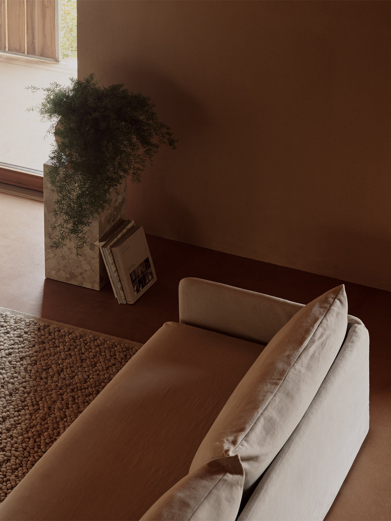 Overhead view of an Offset Sofa with Loose Cover, next to a Gravel Rug, and a Plinth Pedestal with a plant and books.
