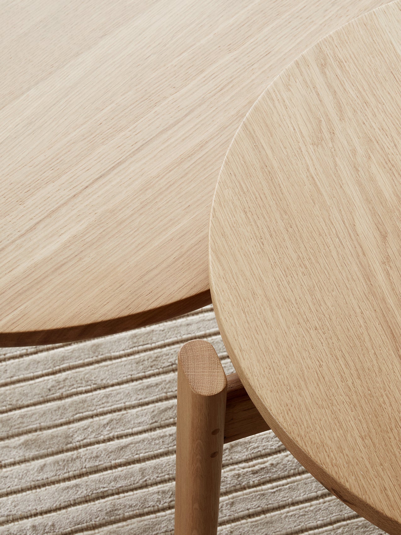 A close-up detail shot of the natural oak Passage Lounge Table's round top and leg, resting on the textured Houkime Rug.
