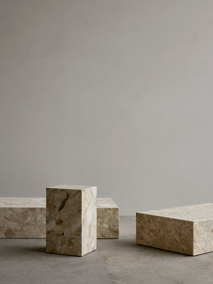 Plinth Grand, Plinth Tall, and Plinth Low tables, crafted from patterned beige marble, on a grey concrete floor.