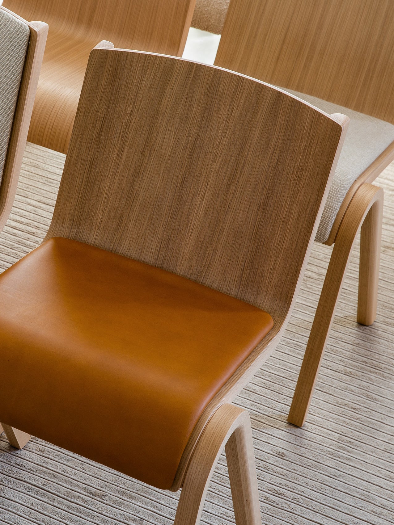 A close-up of the Ready Dining Chair, Seat Upholstered, showing its oak veneer frame and smooth, tan leather seat cushion.