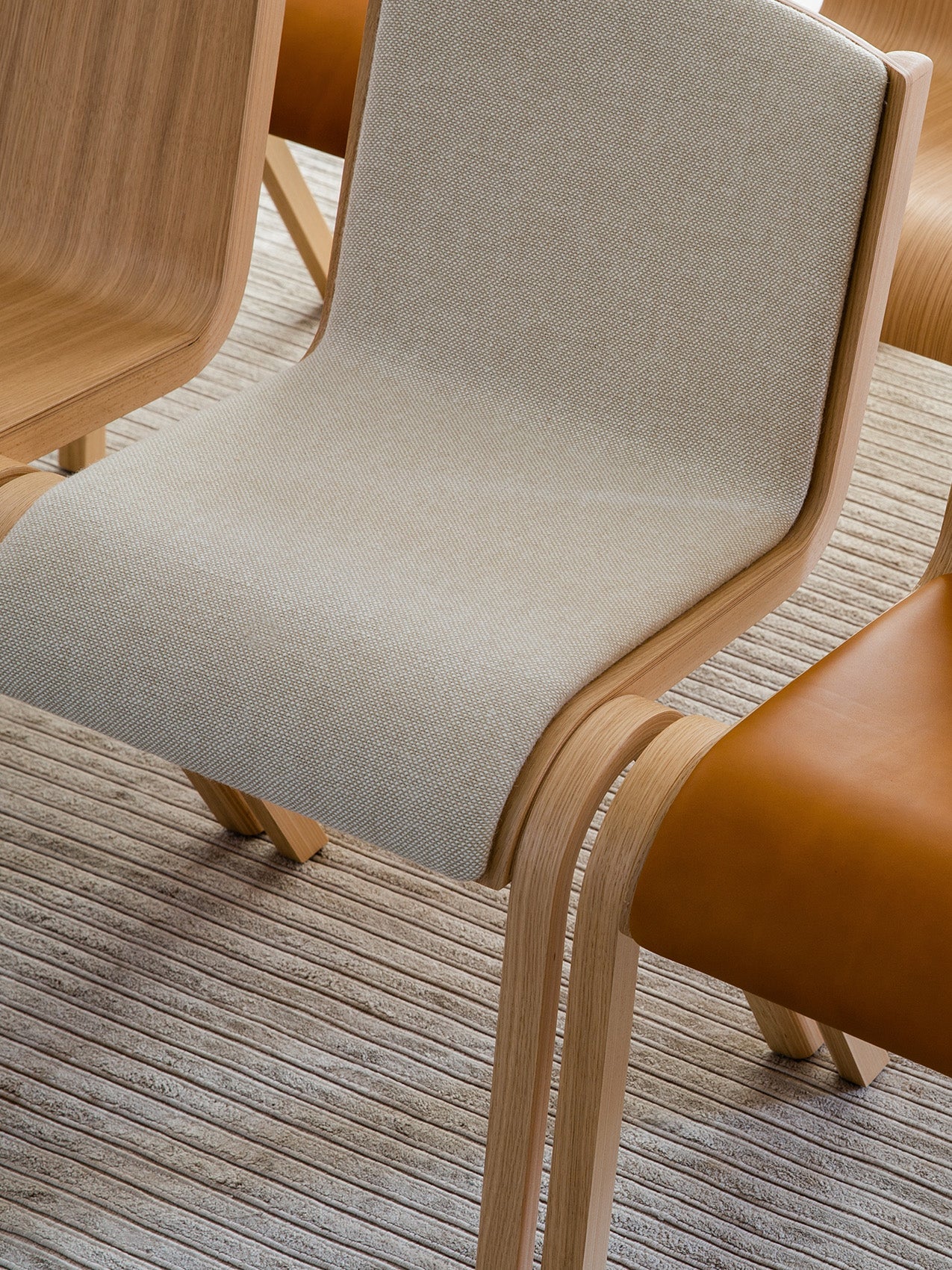 Close-up of the Ready Dining Chair, Front Upholstered, showing its light oak frame and textured beige fabric on a ribbed rug.