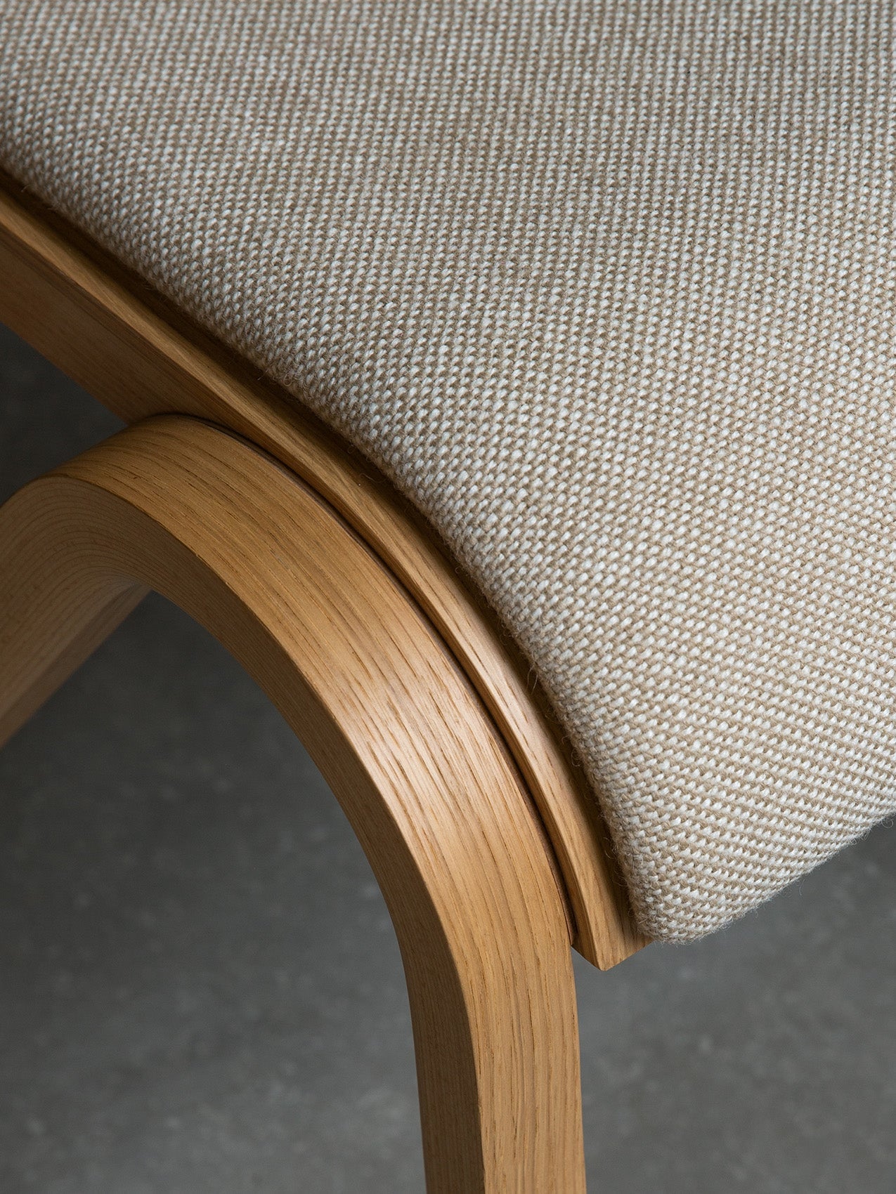 Close-up of the Ready Dining Chair's seat, showing the beige woven upholstery and the grain of the curved oak frame.