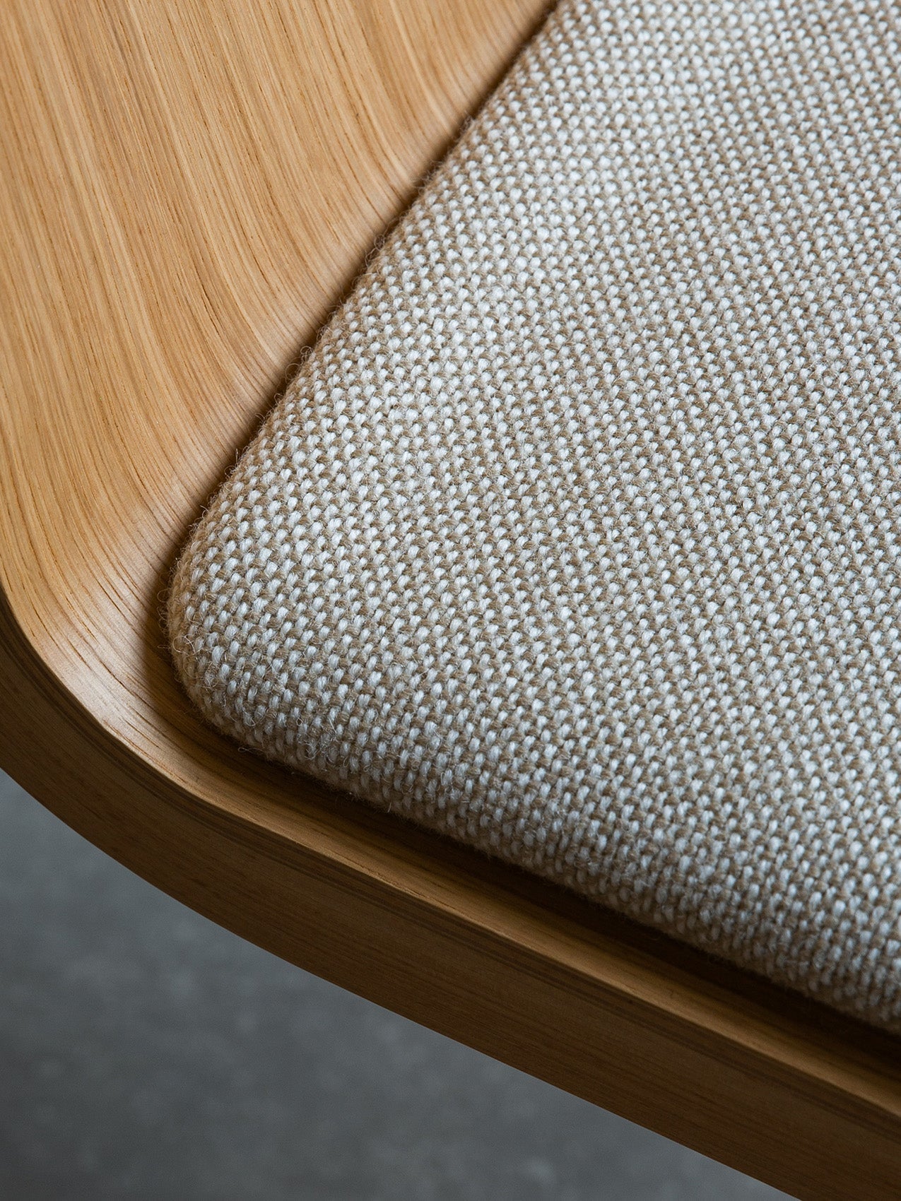 Close-up of the Ready Dining Chair's seat corner, showing textured beige woven upholstery and curved light oak frame.