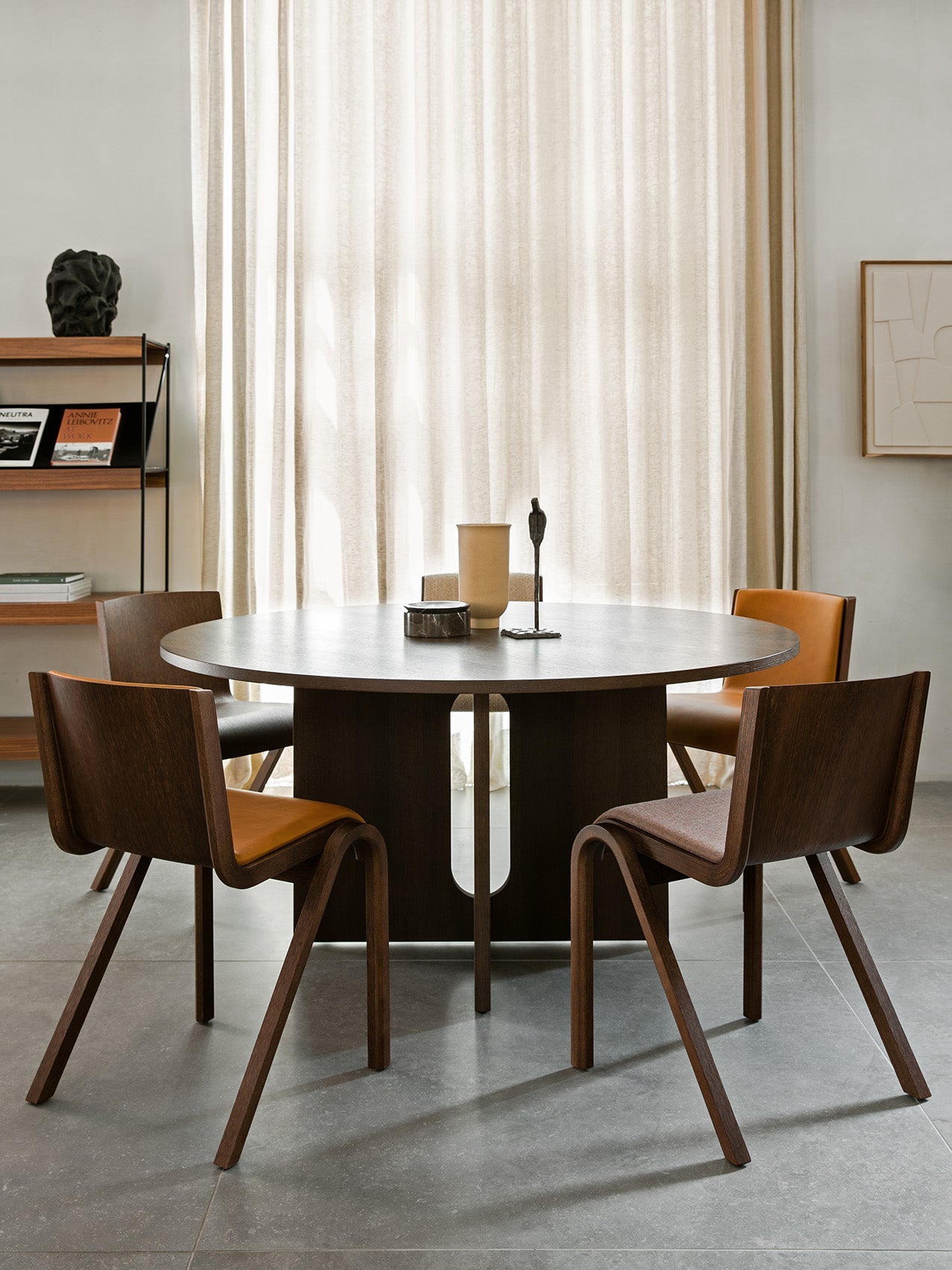 Four Ready Dining Chairs in dark wood with upholstered seats surround a round, dark wood Androgyne Dining Table.