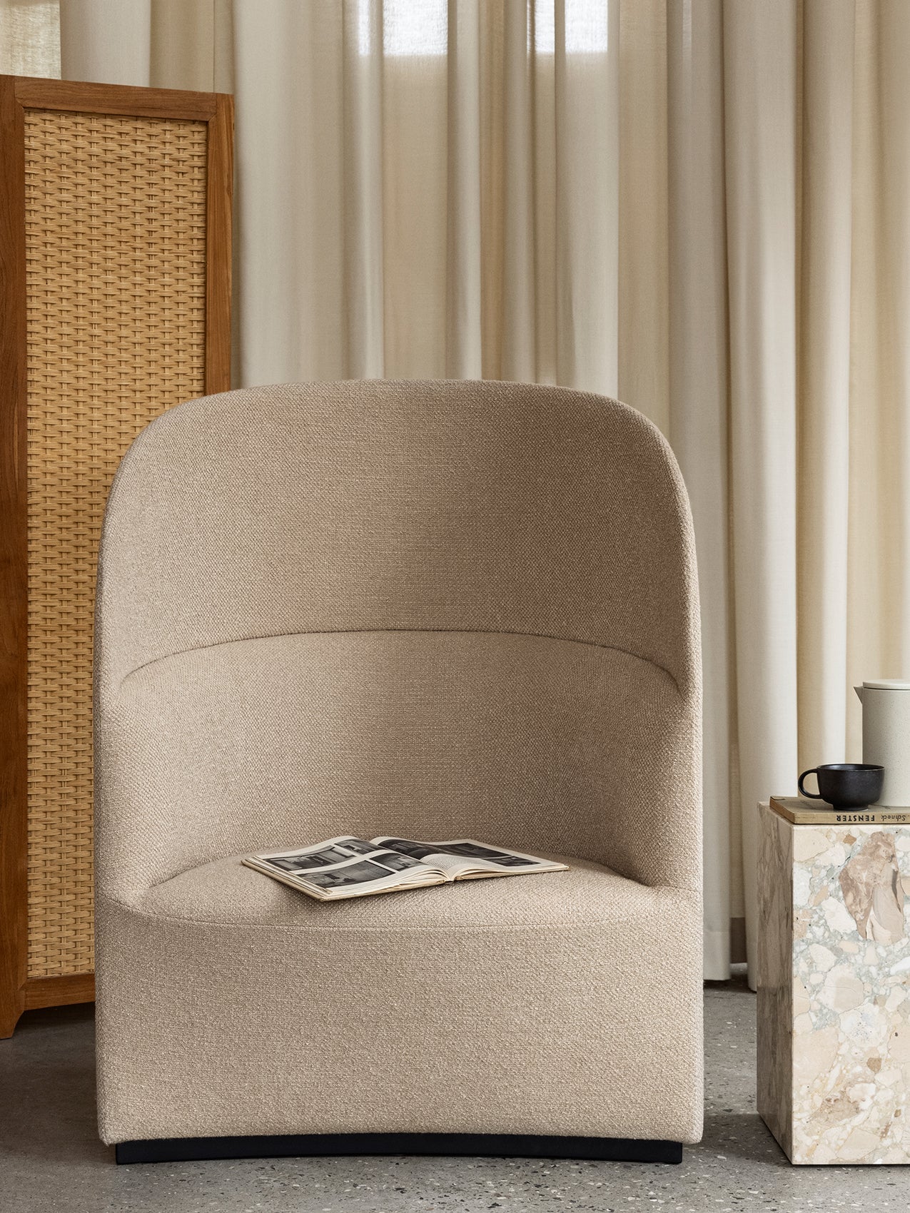 The Tearoom Lounge Chair, High Back in a beige fabric, styled with a marble plinth, a rattan screen, and neutral curtains.