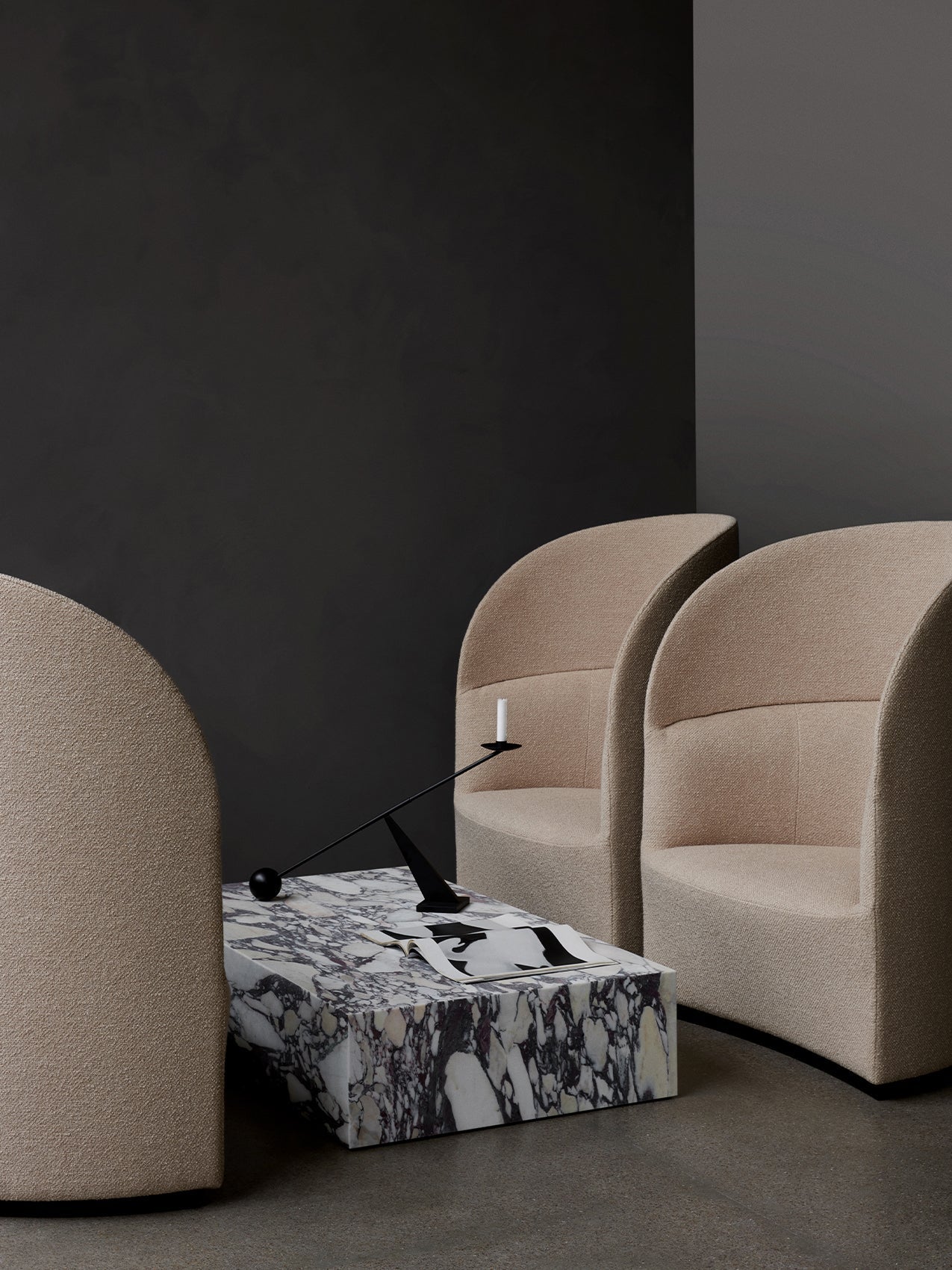 Two beige, high-back Tearoom Lounge Chairs and a Plinth Grand marble table with an Interconnect Candle Holder in a dark room.