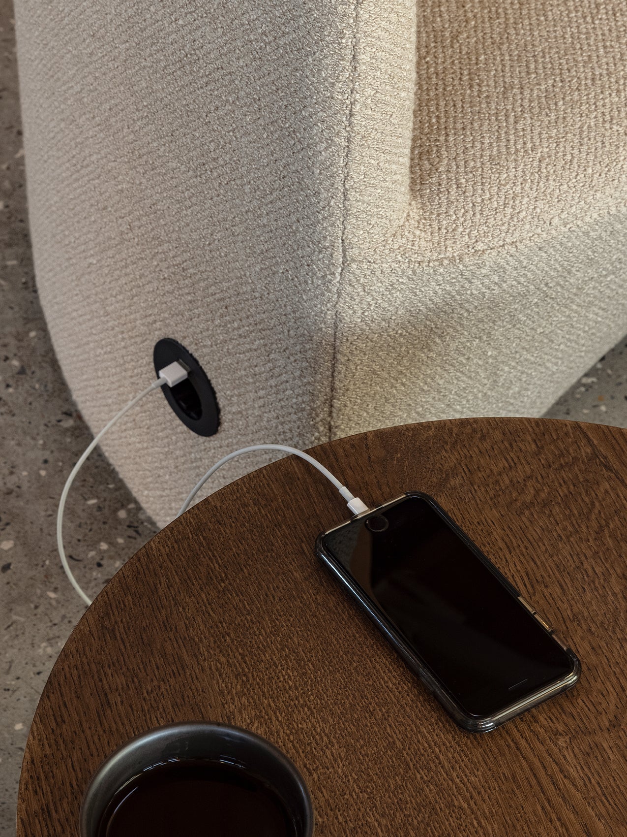 A close-up of the Tearoom Lounge Chair's built-in USB port, with a cable charging a phone on a wooden Androgyne Side Table.