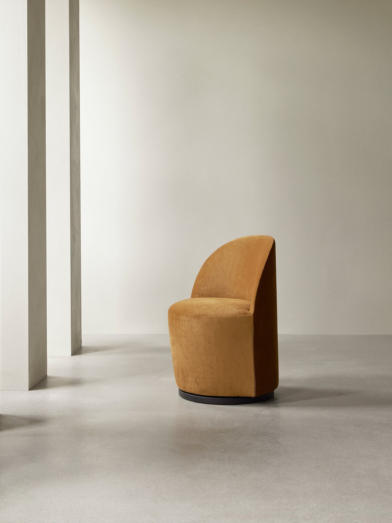 The Tearoom Club Chair, Swivel w/ Return, in mustard-coloured upholstery, sits in a minimalist space with concrete floors.