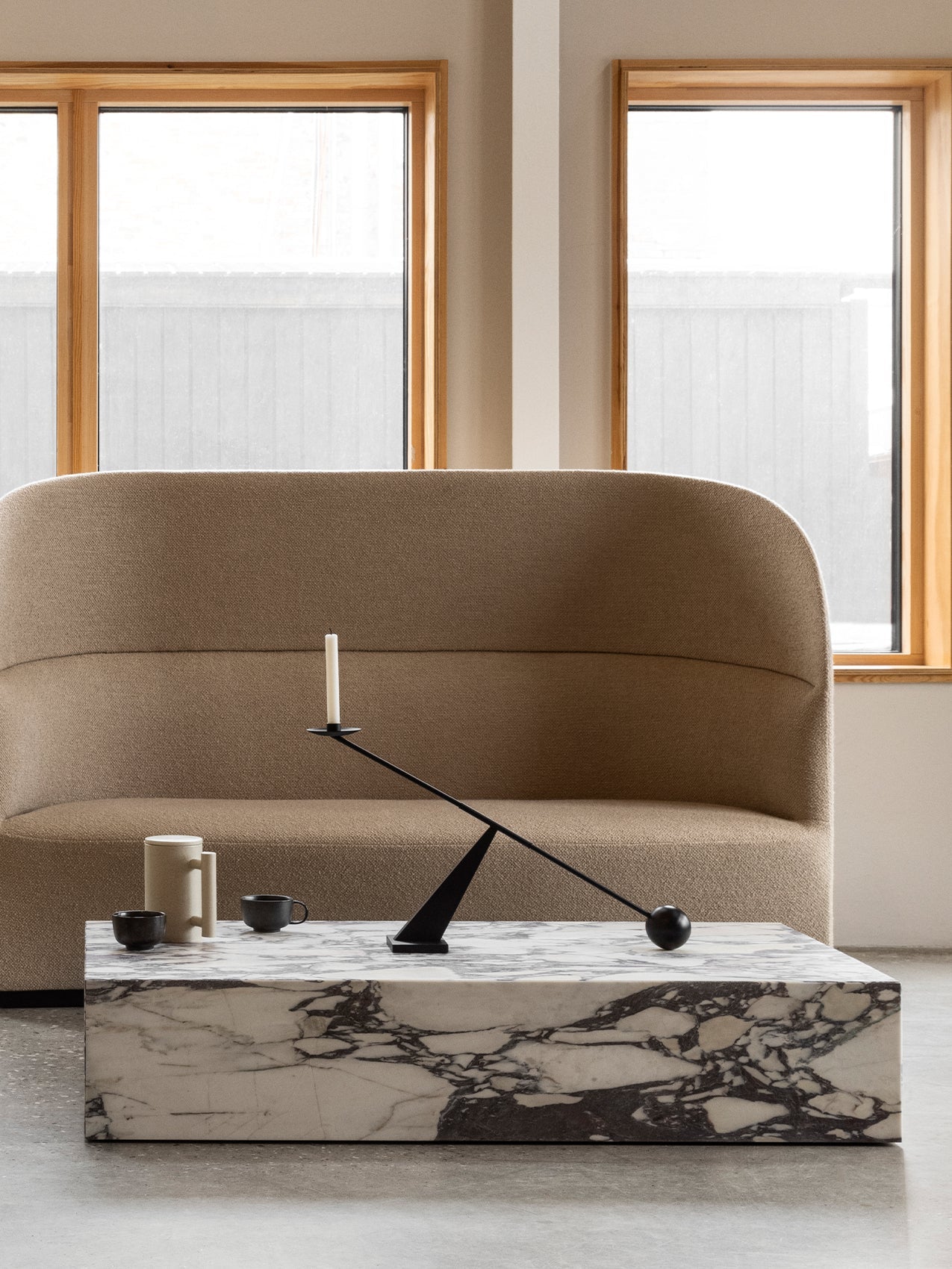 A high-backed Tearoom Sofa in beige fabric. In front, a marble Plinth coffee table holds an Interconnect Candle Holder.