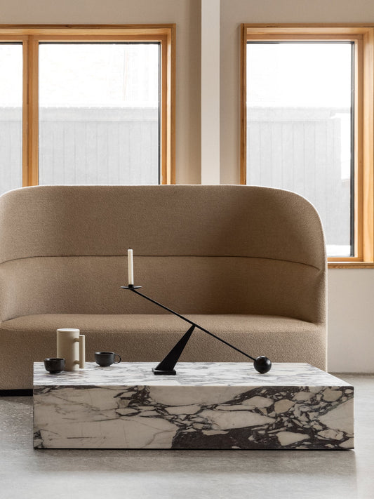 A high-backed Tearoom Sofa in beige fabric. In front, a marble Plinth coffee table holds an Interconnect Candle Holder.