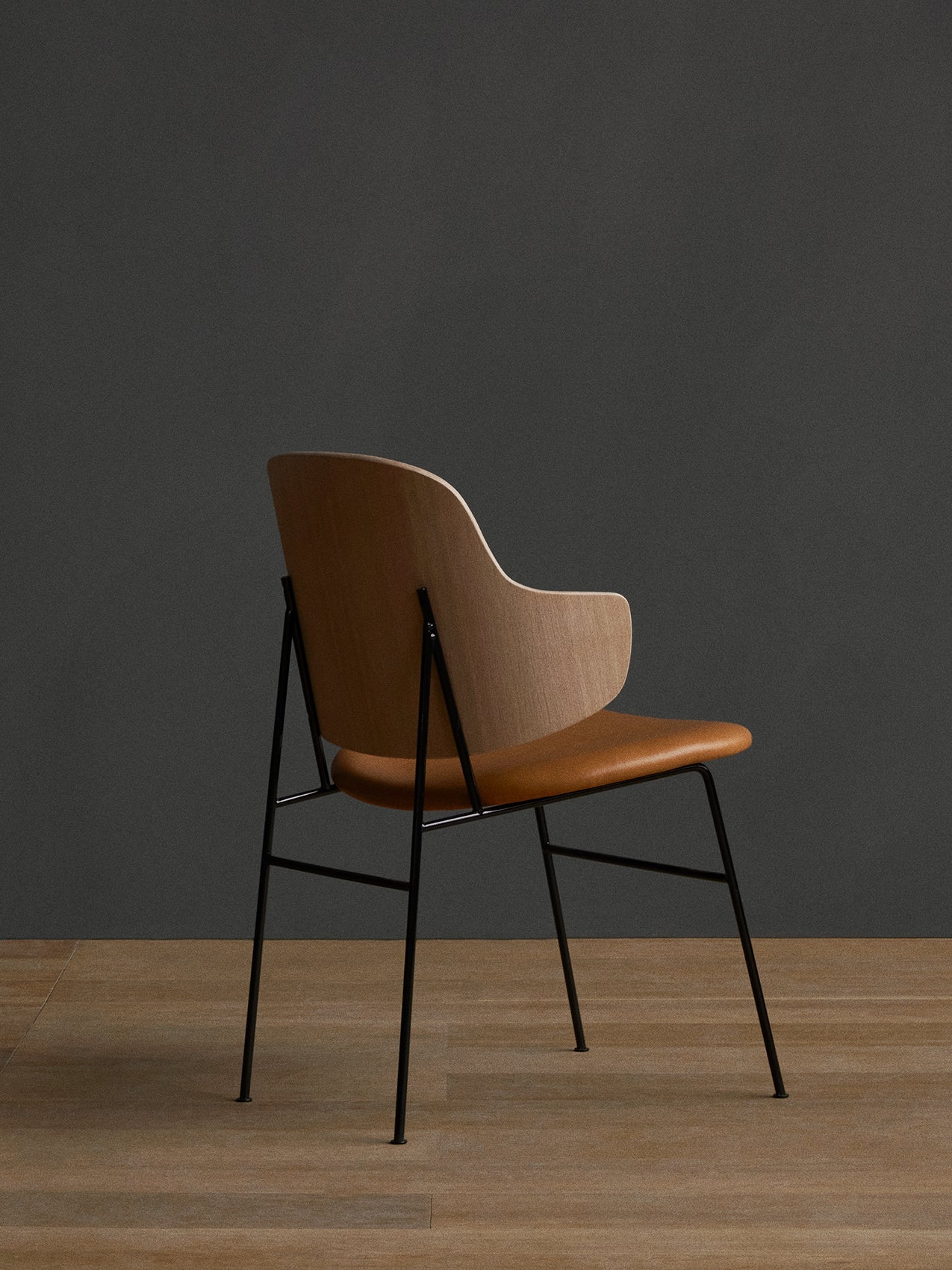 Rear three-quarter view of The Penguin Dining Chair with natural oak back, tan upholstered seat and slender black frame.