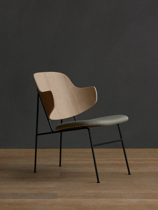 A side view of The Penguin Lounge Chair with a light wood back, grey upholstered seat, and black metal frame on a wood floor.