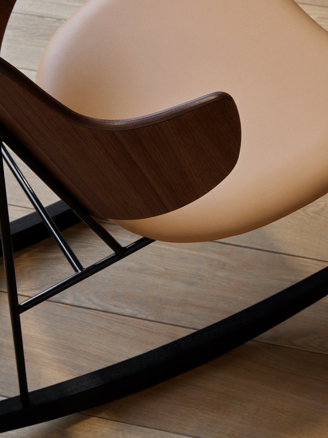 A close-up, high-angle shot of The Penguin Rocking Chair's dark walnut armrest, tan leather seat, and black frame.