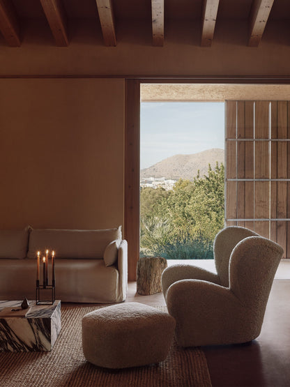 A living room featuring The Tired Man chair, Offset Sofa, Plinth table, and a lit Kubus candle holder, with an open patio.