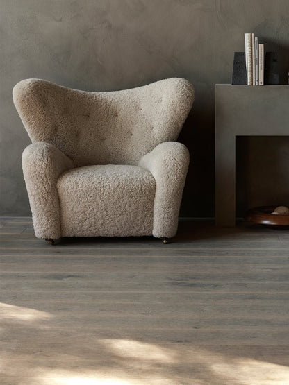 A fluffy, off-white The Tired Man Lounge Chair against a dark grey wall with Converge Book Ends and a Rond Bowl.
