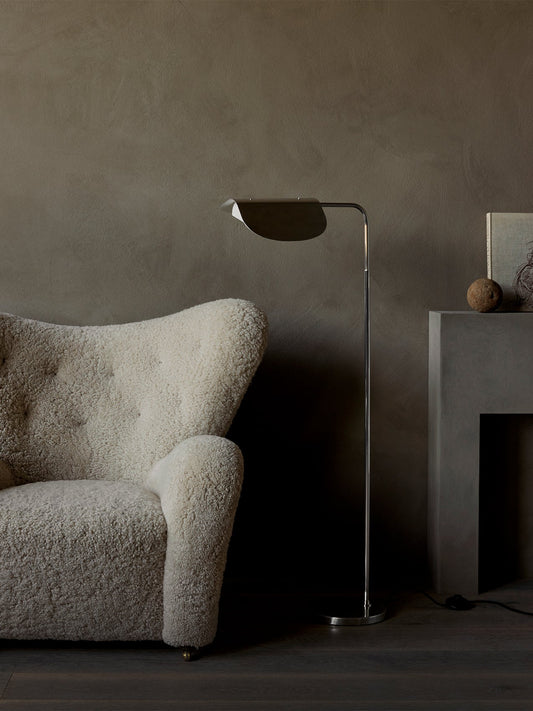 The polished aluminium Wing Floor Lamp stands in a living room beside a cream shearling armchair and a modern grey fireplace.