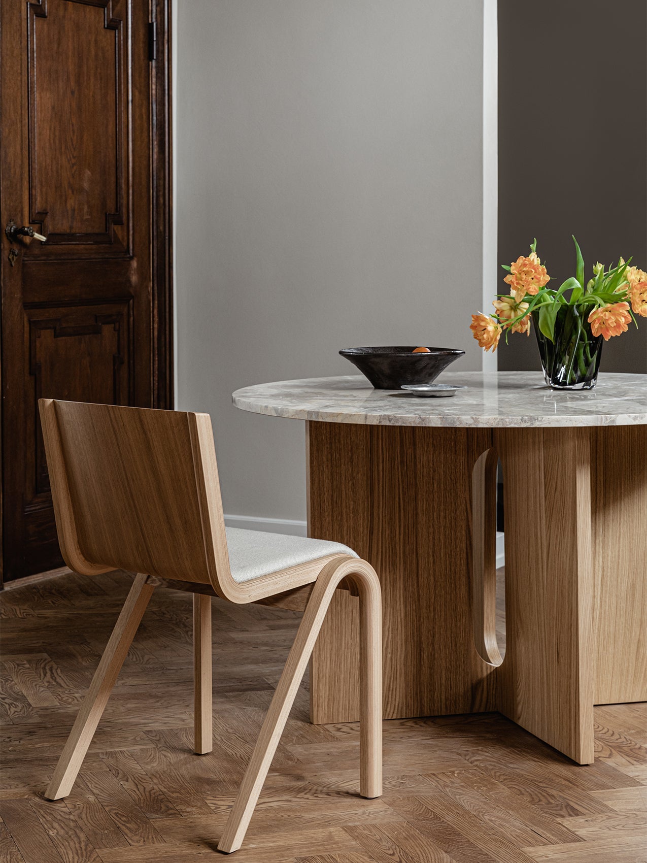 A Ready Dining Chair in light oak at an Androgyne Dining Table with a marble top, styled with a Triptych Bowl and Aer Vase.