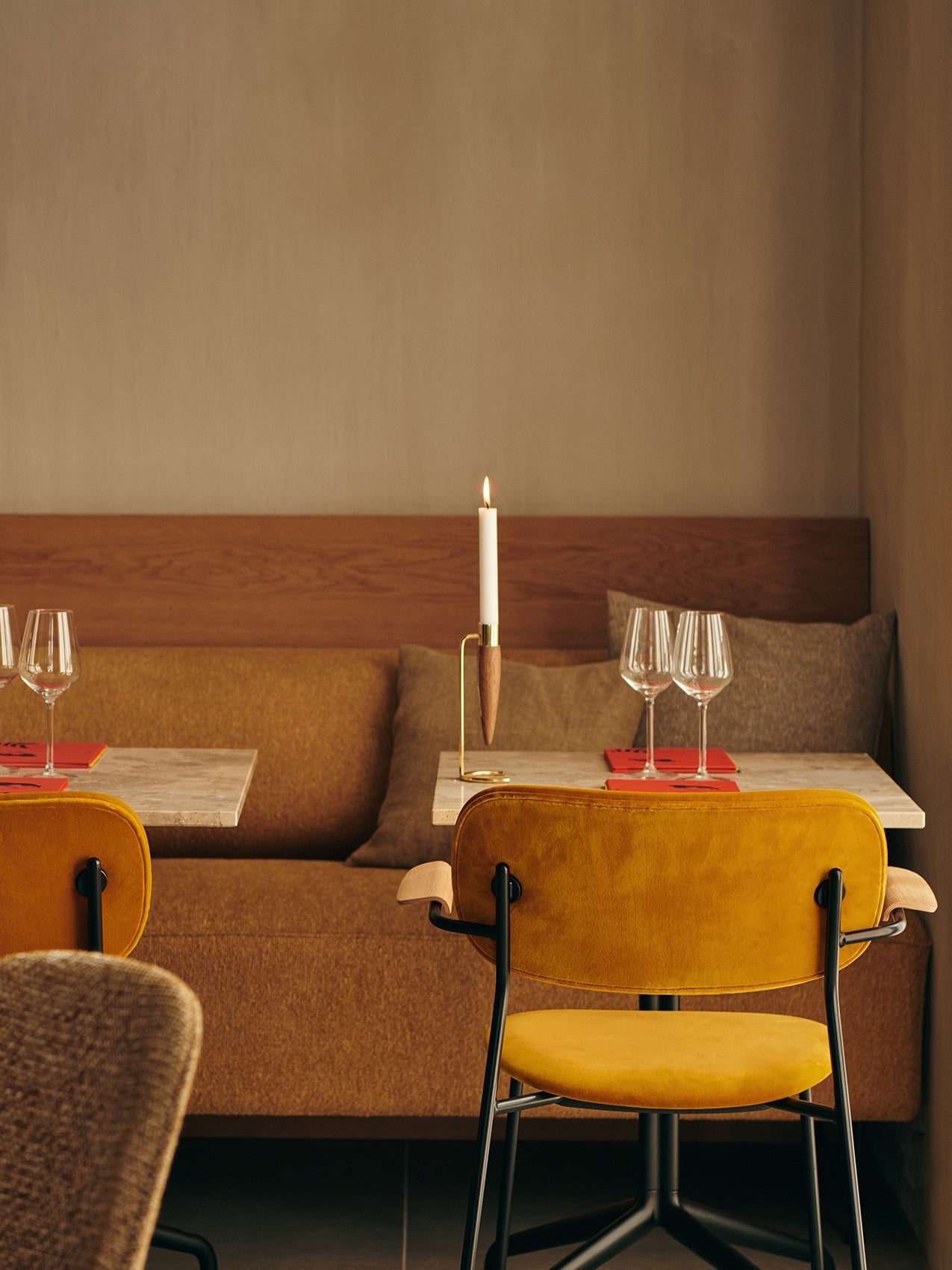 A restaurant with yellow Co Dining Chairs at tables beside an Eave Dining sofa. An Umanoff Candle Holder sits on one table.
