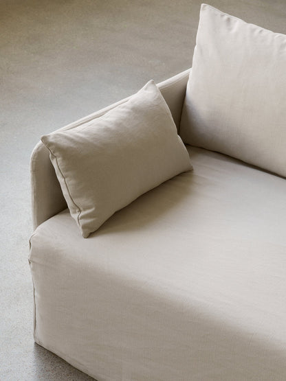 A close-up, high-angle shot of a sofa upholstered in a light beige, textured fabric, with soft cushions, on a concrete floor.