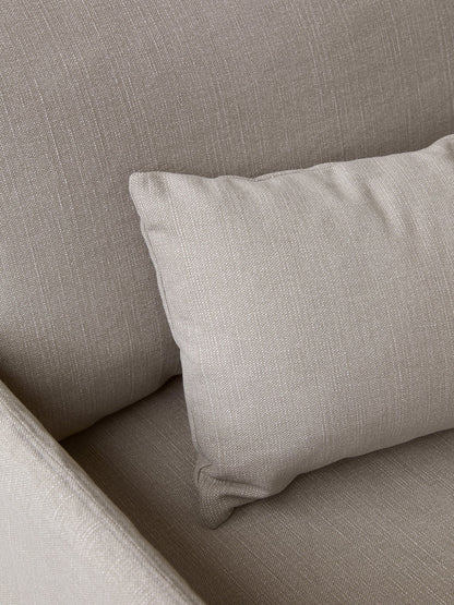 A close-up shot of a beige, textured fabric corner of a sofa or armchair, with a matching cushion resting against the back.