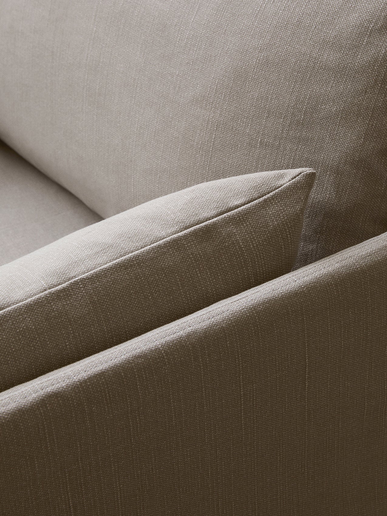 Close-up of a sofa's upholstery in a light brown, textured, woven fabric. The corner of a soft cushion is visible.