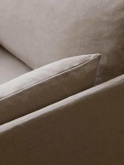 Close-up of a sofa's upholstery in a light brown, textured, woven fabric. The corner of a soft cushion is visible.