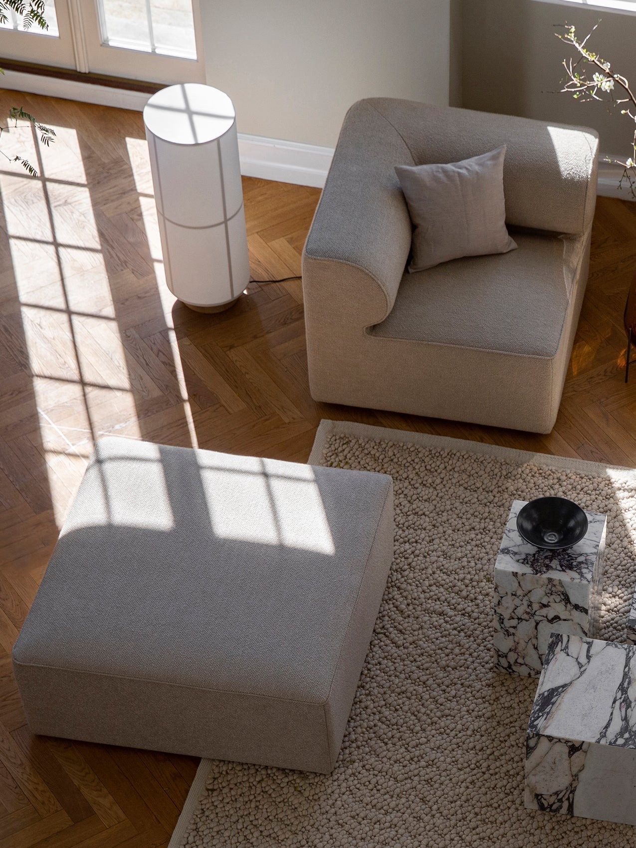 High-angle view of a living room with the Hashira Floor Lamp, modular sofa, and marble plinths on a wooden herringbone floor.
