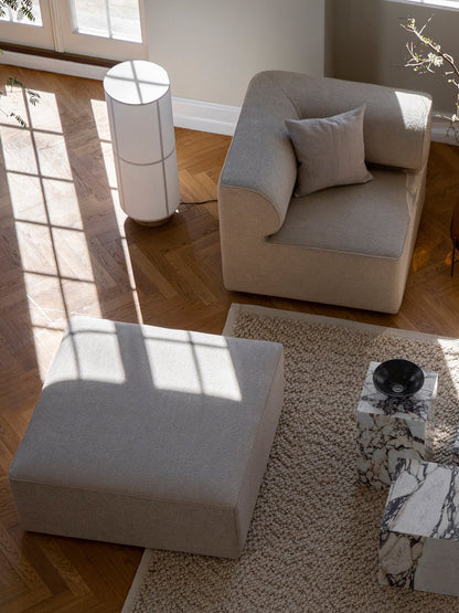 High-angle view of a living room with the Hashira Floor Lamp, modular sofa, and marble plinths on a wooden herringbone floor.