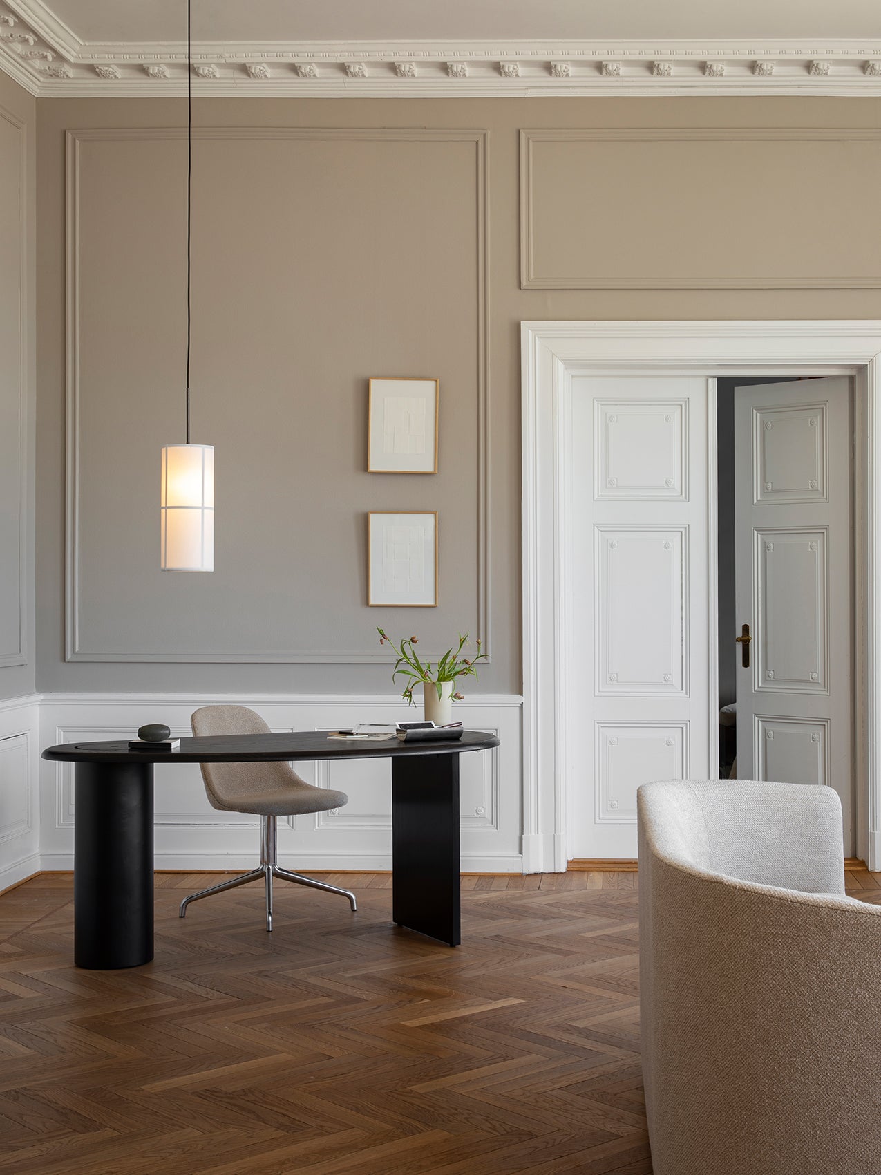 The white Hashira Pendant Lamp hangs over a black desk and chair in a room with beige panelled walls and a herringbone floor.