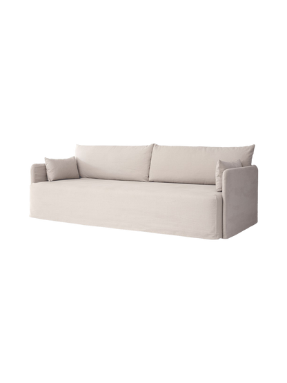 A light-coloured three-seater Offset Sofa w. Loose Cover with two large back cushions and two smaller pillows at the arms.