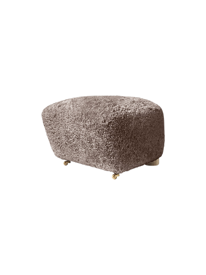 Three-quarter view of The Tired Man Ottoman in Sahara sheepskin, a fluffy footstool with short legs and front brass castors